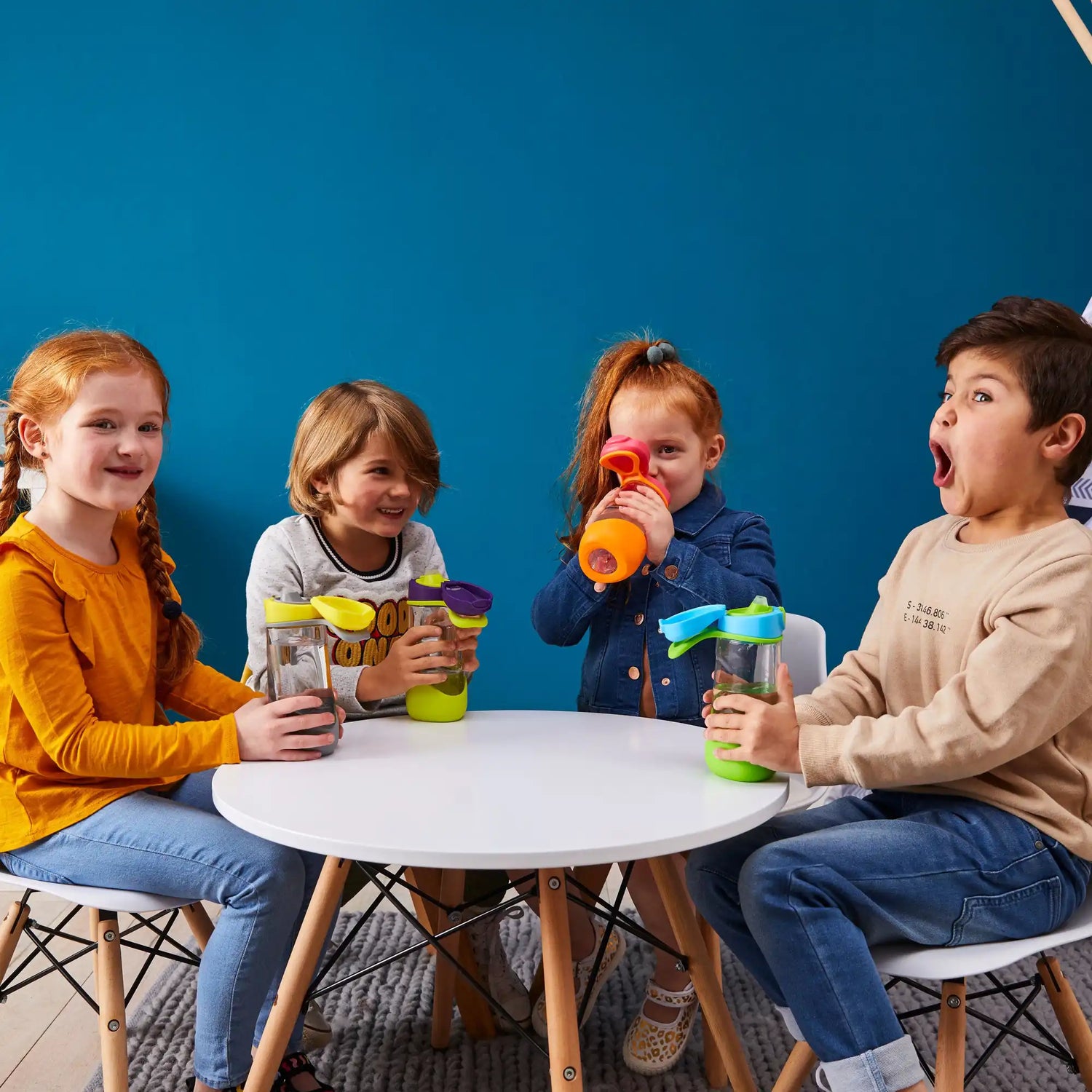 Niños sentados en una mesa blanca redonda bebiendo de tazas coloridas.